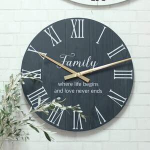 May include: A dark blue wooden clock with Roman numeral markings and gold hands. The clock face has the words "Family, where life begins and love never ends" printed on it.