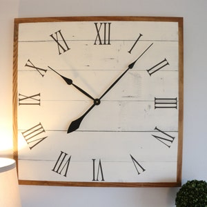 May include: A large, white, wooden clock with Roman numeral markings and black hands. The clock has a distressed, rustic look and is framed in a natural wood.