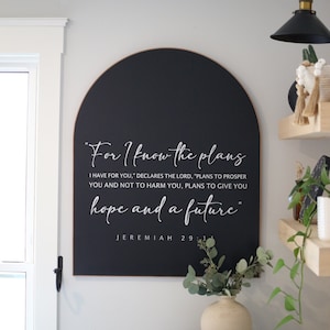 May include: Black arched wooden sign with white text that reads "For I know the plans I have for you," declares the Lord, "plans to prosper you and not to harm you, plans to give you hope and a future." Jeremiah 29:11