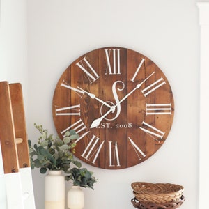 May include: A large, round wooden clock with Roman numeral markings and a white painted initial "S" and the text "EST. 2008".