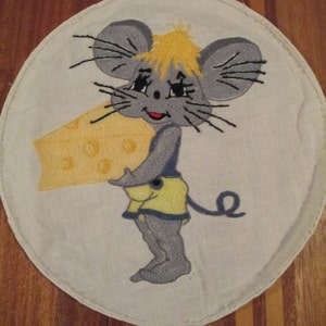 May include: A white embroidered patch with a cartoon mouse holding a wedge of yellow cheese. The mouse has gray fur, black whiskers, and a yellow head.