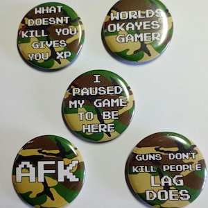 Peut inclure: Cinq boutons ronds avec un motif camouflage. Les boutons ont des phrases différentes imprimées dessus, notamment "What Doesn't Kill You Gives You XP", "Worlds Okayes Gamer", "I Paused My Game To Be Here", "AFK", et "Guns Don't Kill People Lag Does".