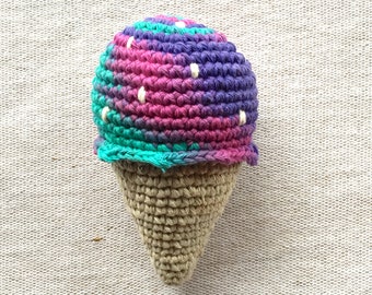 May include: A crocheted ice cream cone toy with a purple, pink, and teal ice cream scoop with white dots. The cone is made of a beige yarn.