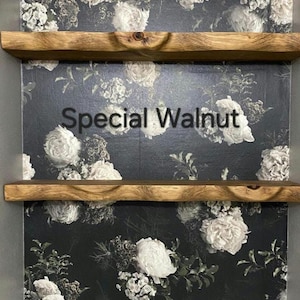May include: Two wooden shelves with a natural wood finish, mounted on a wall with a floral wallpaper. The wallpaper features a dark background with white flowers. The text "Special Walnut" is visible on the wallpaper.