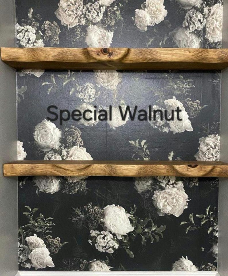 May include: Two wooden shelves with a natural wood finish, mounted on a wall with a floral wallpaper. The wallpaper features a dark background with white flowers. The text "Special Walnut" is visible on the wallpaper.