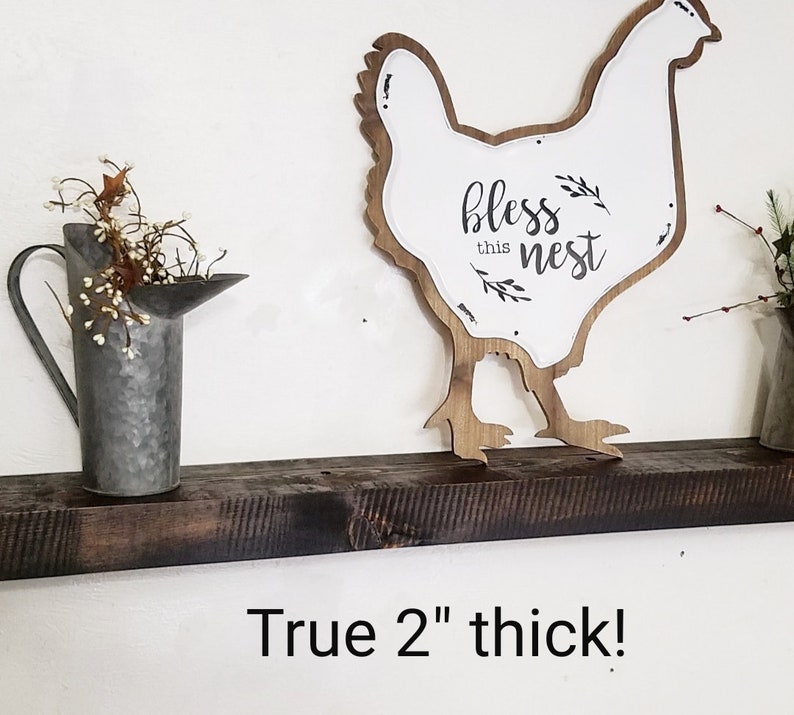 May include: A dark brown wooden shelf with a white chicken silhouette sign that says "bless this nest". The shelf is 2 inches thick.