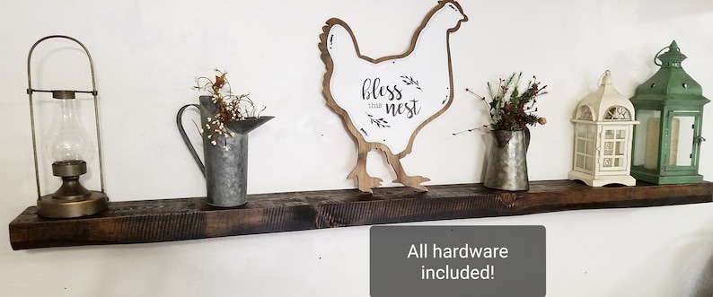 May include: A rustic wooden shelf with a chicken silhouette sign that says "bless this nest". The shelf is decorated with a lantern, a watering can, and two lanterns.