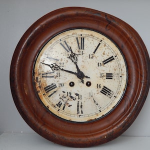 May include: A round, antique clock with a dark brown wooden frame. The clock face is off-white with black Roman numerals and hands. The clock shows signs of age and wear, adding to its vintage appeal.