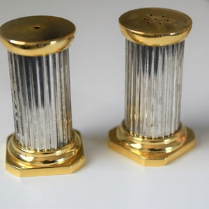 Può includere: Un set di due saliere e pepiere in argento a forma di colonne con accenti dorati.
