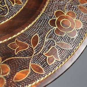 May include: A round wooden serving tray with a decorative floral design. The tray is brown with gold accents and a raised edge.