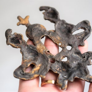 May include: A vintage brass wall decor featuring a stylized design of three figures. The figures are intricately detailed and have a dark patina finish.
