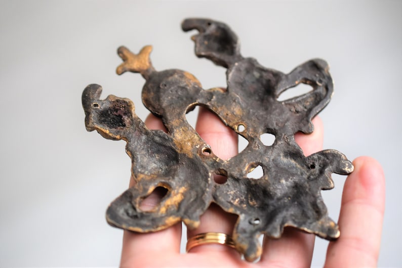 May include: A vintage brass wall decor featuring a stylized design of three figures. The figures are intricately detailed and have a dark patina finish.