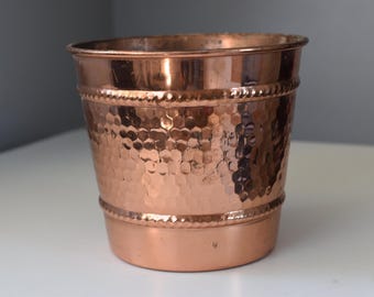 Può includere: Un vaso da fiori in rame martellato con un bordo a perline. Il vaso è di un caldo colore rame e ha un aspetto leggermente usurato.