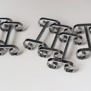 Könnte beinhalten: Satz mit sechs silbernen Serviettenringen aus Metall mit einem gedrehten Design. Jeder Ring hat zwei Schlaufen zum Halten von Servietten.
