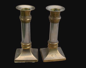 May include: Two silver and gold candle holders with a simple design. The candle holders have a round base and a cylindrical body.