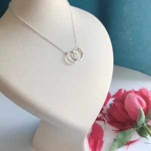 May include: A silver necklace with two interlocking circles as a pendant. The necklace is displayed on a white mannequin bust.