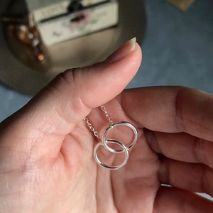 May include: A silver necklace with two interlocking circles as a pendant.