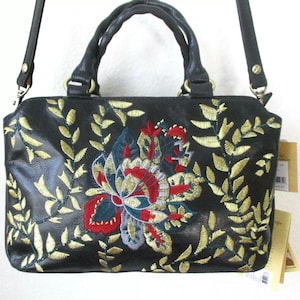 May include: Black handbag with a floral embroidery design. The bag features a large, colorful flower in the center, surrounded by gold-colored leaf embroidery. It has a top handle and a detachable shoulder strap.
