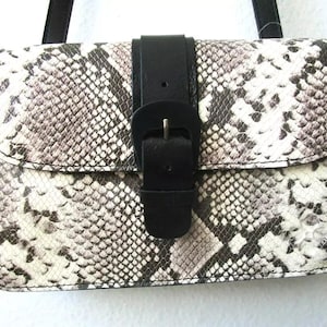 May include: A small, black and white snakeskin patterned handbag with a black leather strap and buckle closure.
