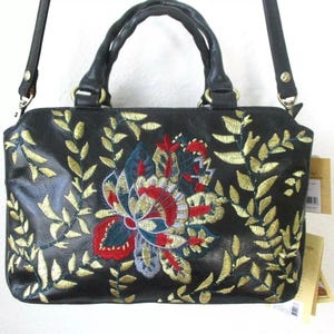 May include: Black handbag with a floral embroidery design. The bag features a central flower with red, blue, and gold accents, surrounded by gold embroidered leaves. It has a top handle and a detachable shoulder strap.