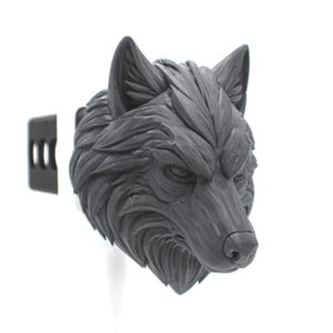 May include: A matte black wolf head sculpture featuring detailed fur texture and pointed ears. The wolf head is attached to a rectangular black mounting bracket with three horizontal slots, designed for attachment to a vehicle hitch receiver.