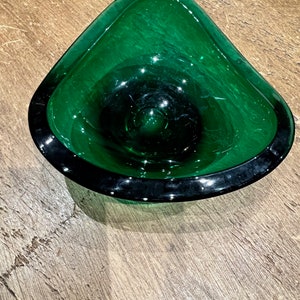 Puede incluir: Un cuenco de vidrio verde con una superficie ondulada y texturizada y un borde negro. El cuenco tiene forma de triángulo con bordes redondeados.
