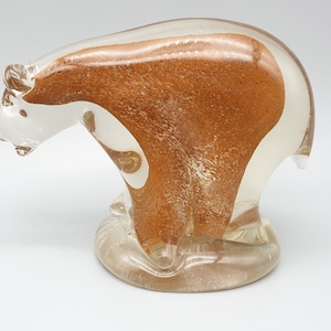Pode incluir: Uma estatueta de urso de vidro transparente com um interior castanho texturizado. O urso está em pose de pé, com a cabeça ligeiramente inclinada. A escultura tem um acabamento liso e brilhante e assenta numa base transparente.
