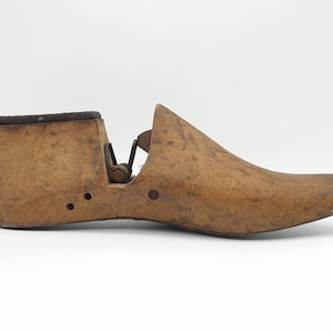 May include: A wooden shoe last with a hinged opening. The last is made of brown wood and has a worn finish. It is used for shaping shoes.