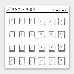 May include: Sheet of white stickers featuring black and white illustrations of iPads. The stickers have a simple outline design with a screen and a diagonal line representing the display. The text "salt + sigil" and "foiled | ipads" are also present.