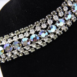 May include: A silver and crystal rhinestone bracelet with iridescent stones. The bracelet is on a black velvet display stand.