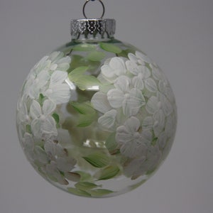 Könnte beinhalten: Transparenter Weihnachtsbaumschmuck aus Glas, verziert mit weißen Blumen und grünen Blättern. Der Schmuck hat eine silberne Metallkappe und eine Schlaufe zum Aufhängen. Das florale Design ist handbemalt und sorgt für einen einzigartigen, festlichen Look.