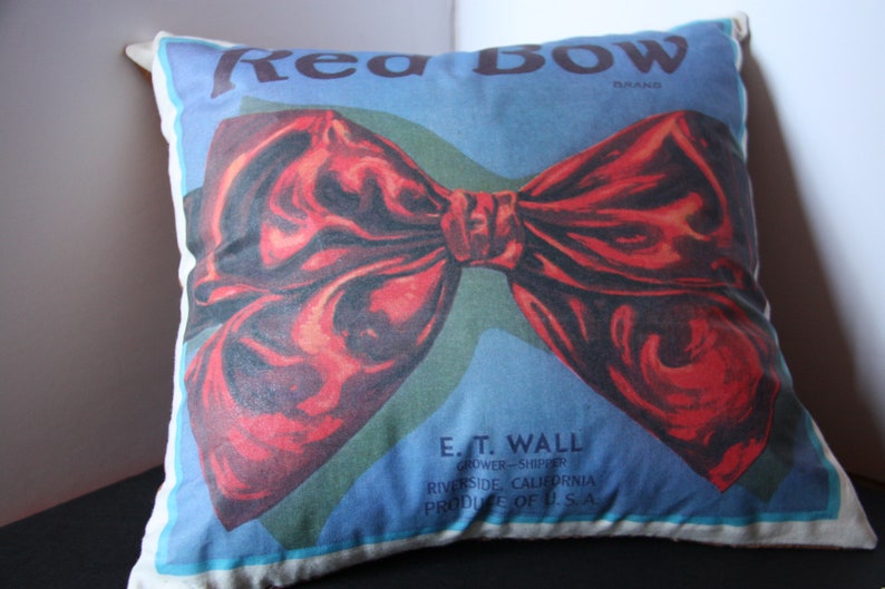 K&ouml;nnte beinhalten: Ein Dekokissen mit einem roten Schleifendesign und dem Text "Red Bow Brand" und "E.T. Wall Grower-Shipper Riverside, Kalifornien Produce of U.S.A."