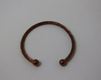 May include: A copper-colored cuff bracelet with a twisted rope design. The open ends of the bracelet have small, round, copper-colored ball terminals. The bracelet is displayed on a white surface.