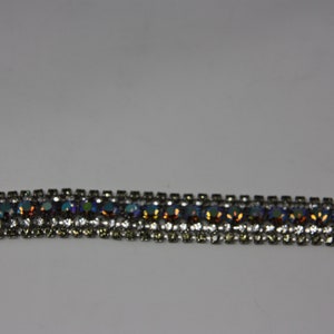 May include: A silver bracelet with a row of iridescent blue, green, and orange rhinestones.