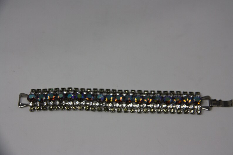 May include: A silver bracelet with a row of iridescent blue, green, and orange rhinestones.