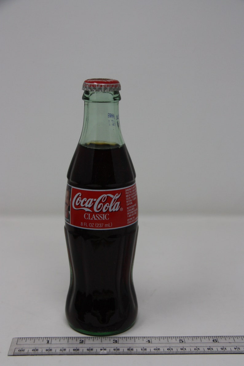 May include: A glass bottle of Coca-Cola Classic, 8 fl oz (237 ml), with a red label and a green cap.