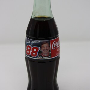 May include: A glass bottle of Coca-Cola with a red and white label featuring Dale Jarrett and the number 88. The label also includes the text "Coca-Cola Classic" and "8 fl oz".