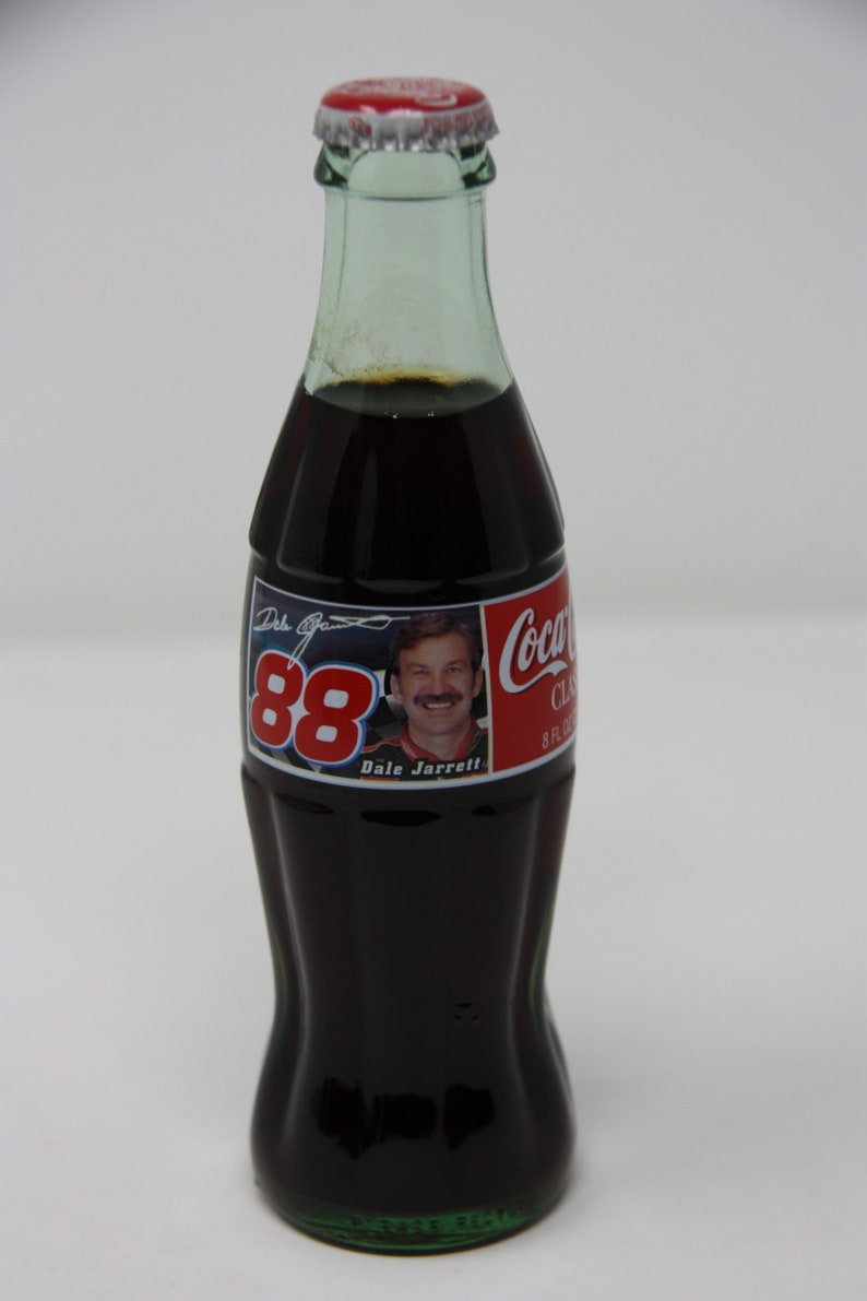 May include: A glass bottle of Coca-Cola with a red and white label featuring Dale Jarrett and the number 88. The label also includes the text "Coca-Cola Classic" and "8 fl oz".