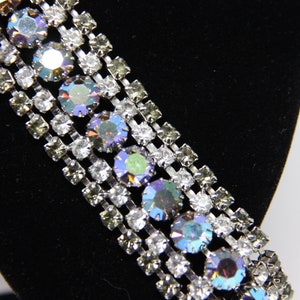 May include: A silver chain with multiple rows of clear and iridescent rhinestones. The chain is on a black background.