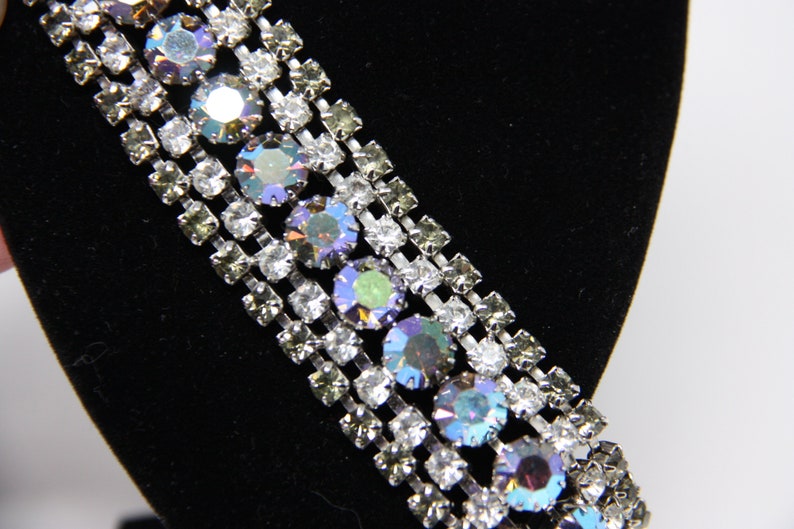 May include: A silver chain with multiple rows of clear and iridescent rhinestones. The chain is on a black background.