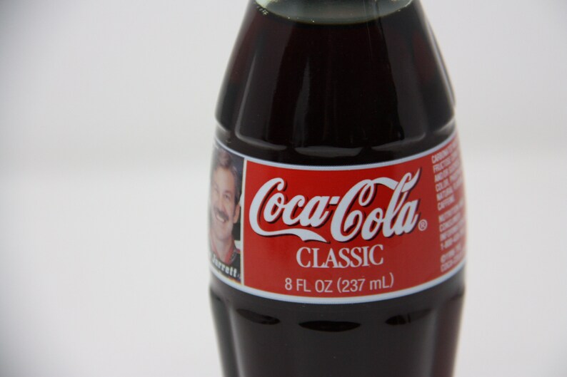 May include: A glass bottle of Coca-Cola Classic soda. The bottle is dark brown and has a red label with the Coca-Cola logo and the words "Classic" and "8 fl oz (237 ml)".