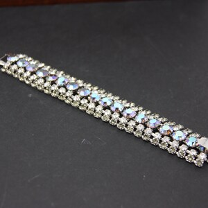 May include: A silver bracelet with a row of iridescent blue and clear rhinestones.