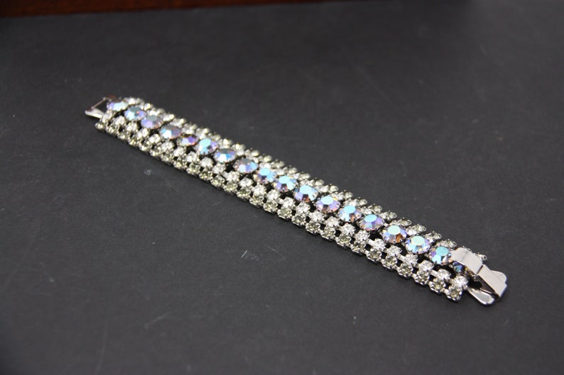 May include: A silver bracelet with a row of iridescent blue and clear rhinestones.