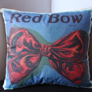 K&ouml;nnte beinhalten: Ein wei&szlig;es Kissen mit einem roten Schleifenmuster. Auf dem Kissen steht "Red Bow Brand" gedruckt.