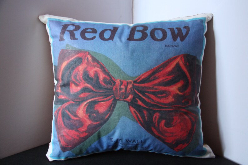 K&ouml;nnte beinhalten: Ein wei&szlig;es Kissen mit einem roten Schleifenmuster. Auf dem Kissen steht "Red Bow Brand" gedruckt.