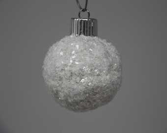 May include: A white Christmas bauble covered in glitter with a silver top.
