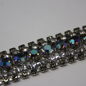 May include: A silver chain with iridescent blue and clear rhinestones. The chain is made of metal and has a repeating pattern of alternating rhinestones.
