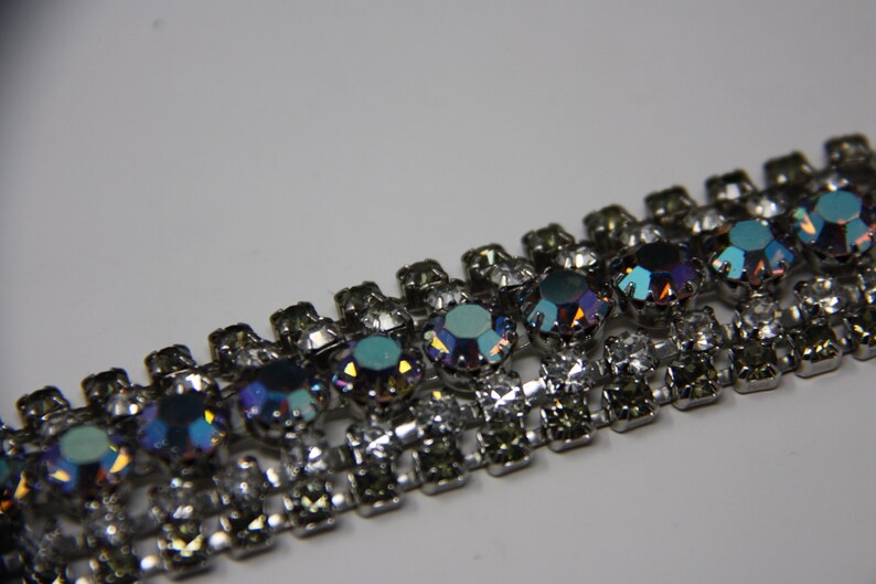 May include: A silver chain with iridescent blue and clear rhinestones. The chain is made of metal and has a repeating pattern of alternating rhinestones.