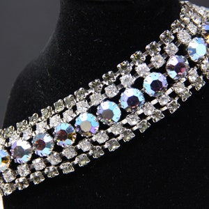 May include: A silver bracelet with a row of iridescent blue and purple rhinestones set in a silver chain.