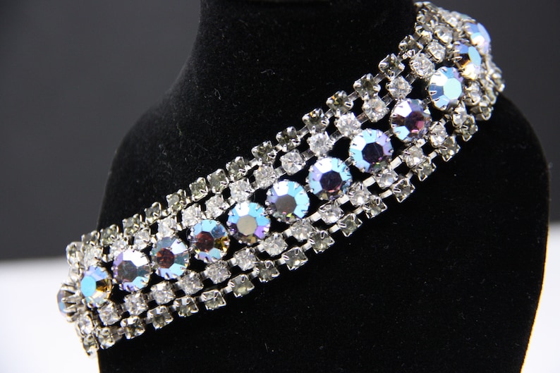 May include: A silver bracelet with a row of iridescent blue and purple rhinestones set in a silver chain.